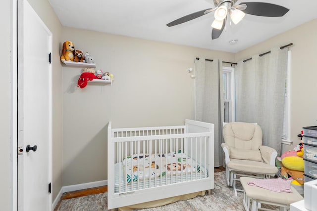 bedroom with a ceiling fan, baseboards, a crib, and wood finished floors