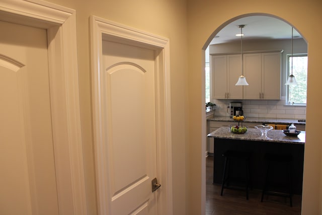 kitchen with a kitchen breakfast bar, backsplash, arched walkways, dark wood finished floors, and dark stone counters