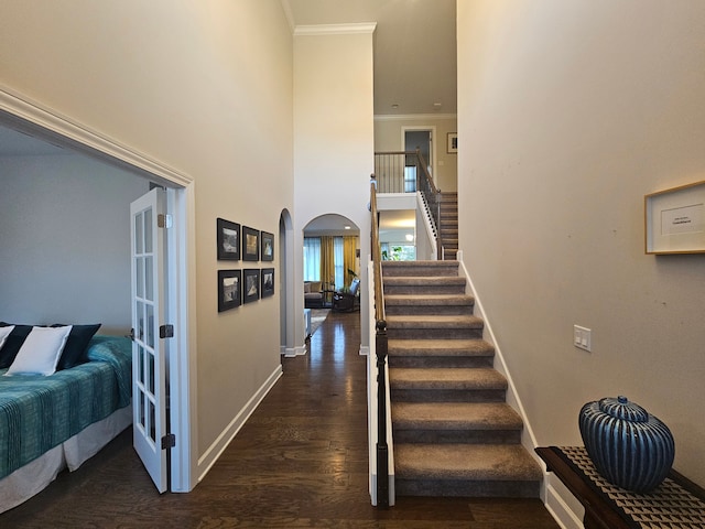 stairs with crown molding, arched walkways, wood finished floors, baseboards, and a high ceiling