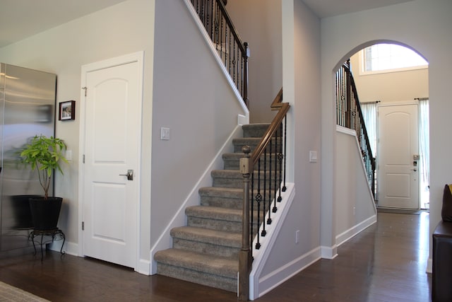 foyer entrance with stairway, arched walkways, baseboards, and dark wood-style flooring