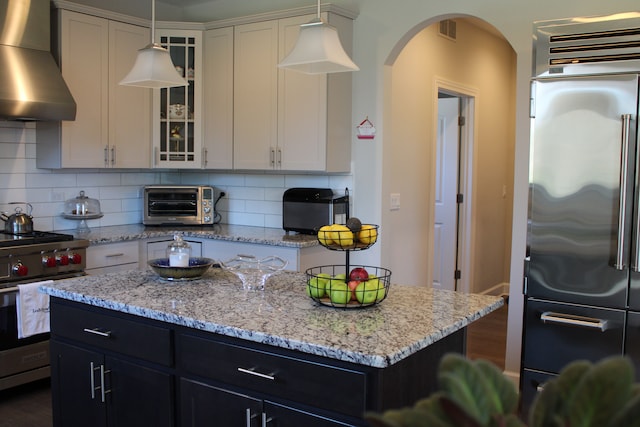 kitchen with visible vents, a toaster, wall chimney range hood, arched walkways, and premium appliances