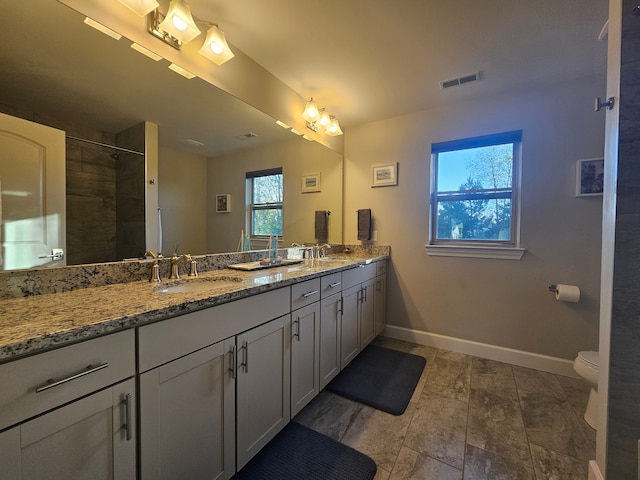 bathroom with double vanity, visible vents, a sink, baseboards, and toilet