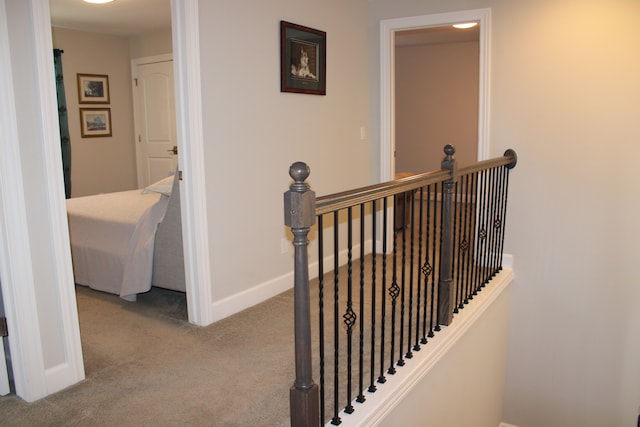 hallway featuring carpet floors, baseboards, and an upstairs landing