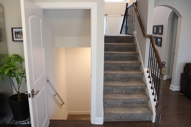 stairway featuring baseboards, arched walkways, and wood finished floors