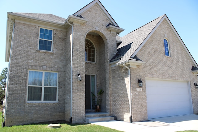 traditional home with brick siding, a shingled roof, an attached garage, and driveway
