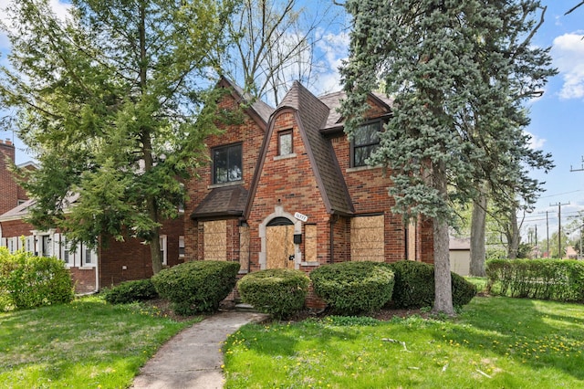 tudor home featuring brick siding, a shingled roof, and a front lawn
