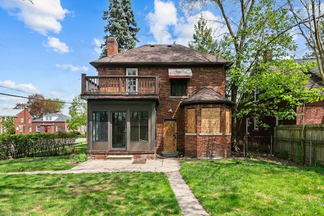 rear view of property featuring fence, a balcony, a chimney, brick siding, and a lawn
