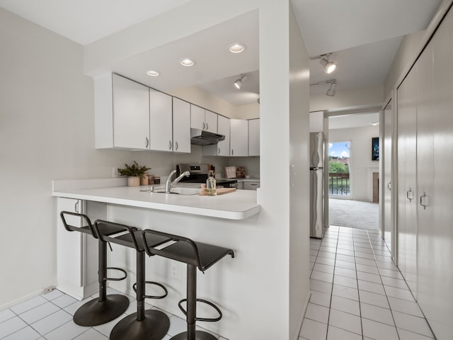 kitchen featuring a sink, light countertops, under cabinet range hood, a breakfast bar, and stainless steel appliances