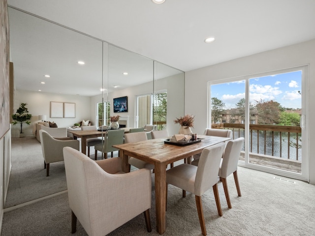 dining space with a water view, recessed lighting, light colored carpet, and visible vents