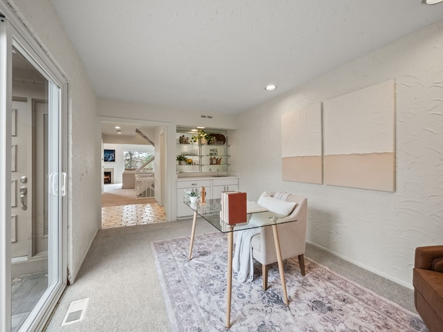 office space featuring visible vents, a textured wall, light carpet, a lit fireplace, and recessed lighting