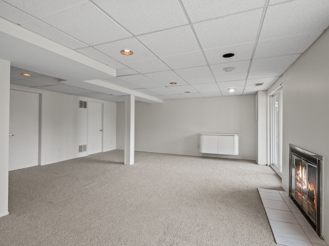 below grade area with light colored carpet, a fireplace with flush hearth, a paneled ceiling, and visible vents
