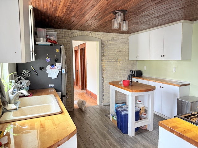 kitchen featuring white cabinets, a sink, butcher block countertops, freestanding refrigerator, and wood ceiling
