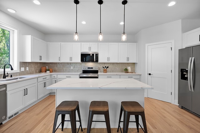 kitchen with appliances with stainless steel finishes, a sink, a kitchen bar, decorative backsplash, and white cabinets
