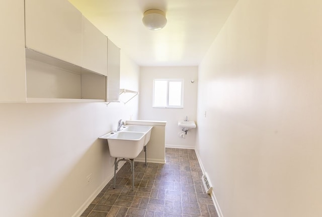 laundry area featuring a sink, baseboards, brick patterned floor, and visible vents