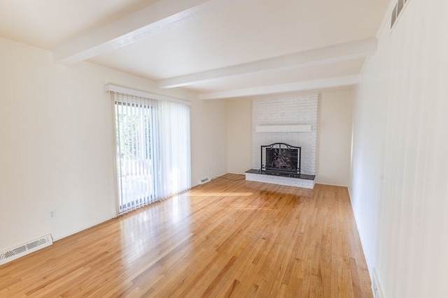 unfurnished living room with visible vents, light wood-style floors, beam ceiling, and a fireplace
