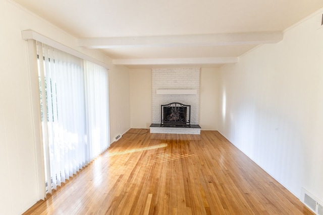 unfurnished living room with light wood-style floors, a brick fireplace, beam ceiling, and visible vents