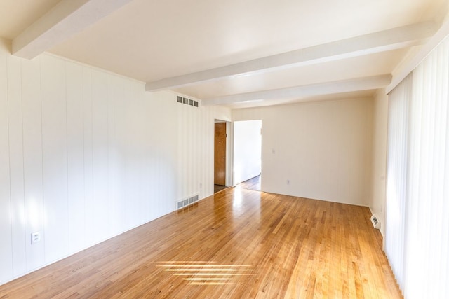 unfurnished room with visible vents, light wood-type flooring, and beamed ceiling
