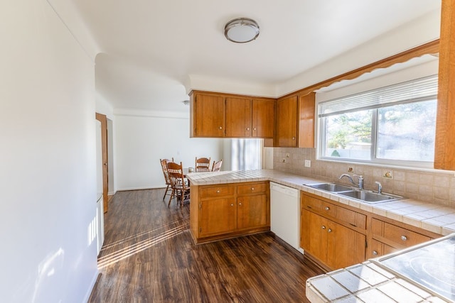 kitchen with white dishwasher, a sink, tile counters, a peninsula, and dark wood-style floors