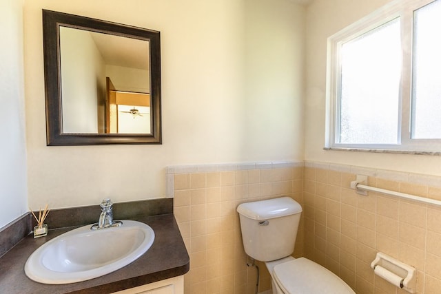bathroom featuring vanity, a wainscoted wall, toilet, and tile walls
