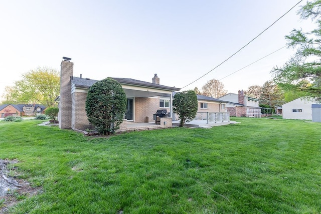 back of property featuring a lawn, a patio, a chimney, and brick siding
