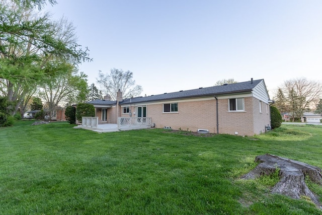 back of house featuring brick siding, a lawn, a chimney, and a patio