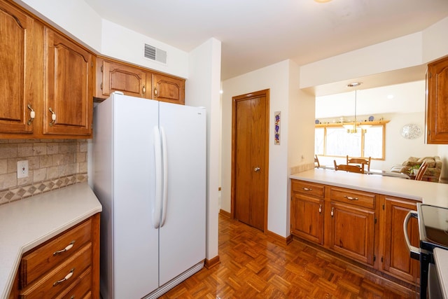 kitchen with visible vents, freestanding refrigerator, decorative backsplash, light countertops, and brown cabinets