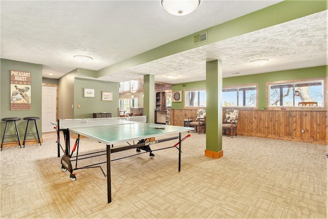 rec room with visible vents, a textured ceiling, wooden walls, and light carpet