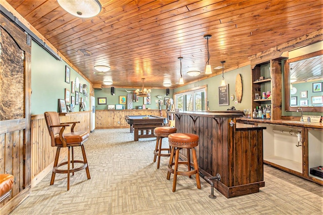 bar with light colored carpet, wainscoting, a sink, wood ceiling, and a bar