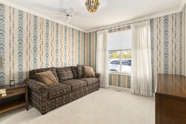 living room featuring ceiling fan, visible vents, carpet floors, ornamental molding, and wallpapered walls