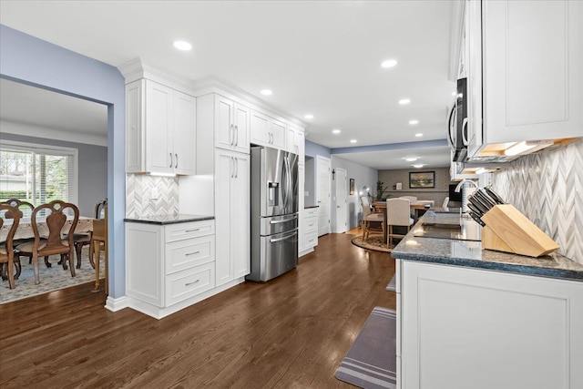 kitchen with appliances with stainless steel finishes, backsplash, dark wood-style flooring, and white cabinetry