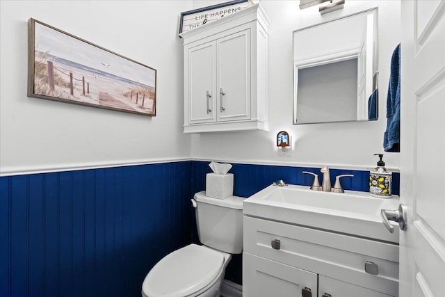 bathroom with a wainscoted wall, vanity, and toilet