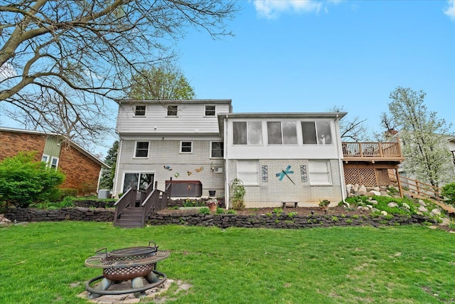 back of property with a lawn, a wooden deck, a sunroom, brick siding, and a fire pit