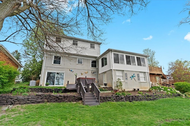 back of property featuring brick siding, a sunroom, a yard, and a deck