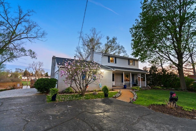 view of front of home featuring a porch, a chimney, a lawn, brick siding, and aphalt driveway