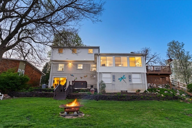 rear view of house with a wooden deck, a yard, an outdoor fire pit, and brick siding