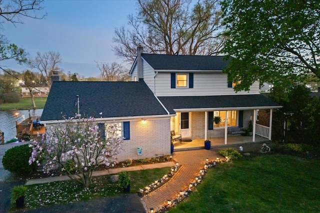 back of house with a porch, a chimney, a lawn, brick siding, and a shingled roof