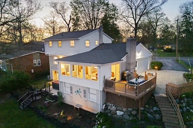 back of house at dusk with stairway, a chimney, a shingled roof, and a wooden deck