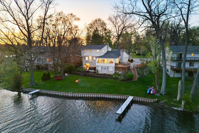 back of property at dusk with a deck with water view and a yard
