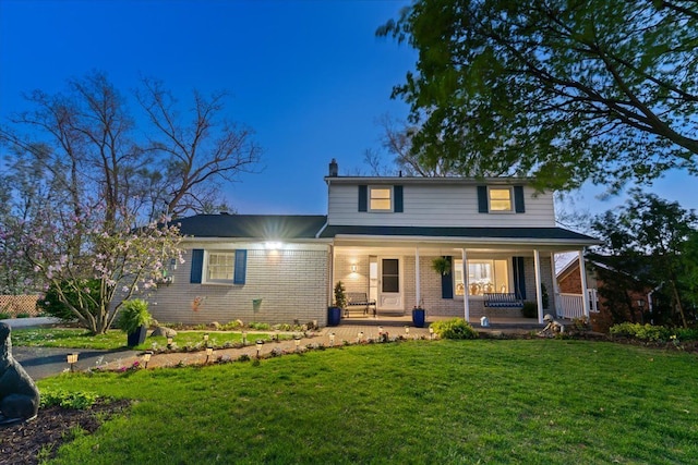 view of front of house with covered porch, brick siding, a chimney, and a front lawn