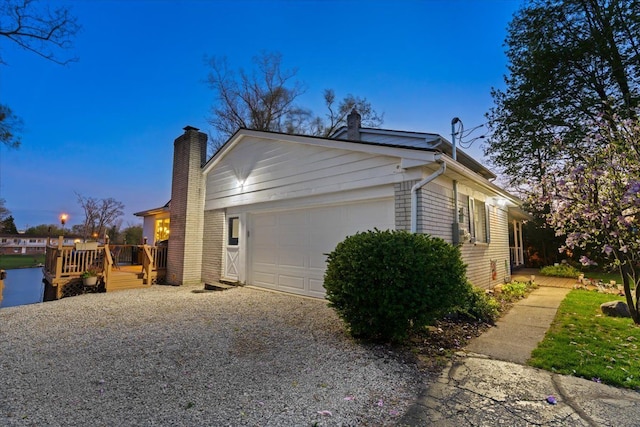 view of side of home with brick siding, a garage, a deck, a chimney, and driveway