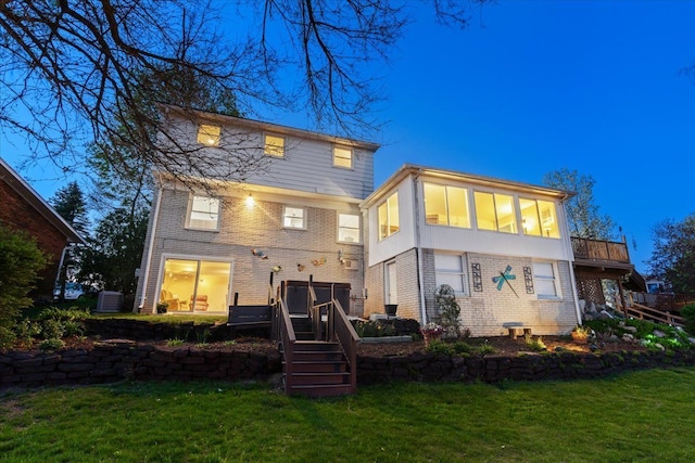 back of property featuring a lawn, brick siding, a wooden deck, and stairs