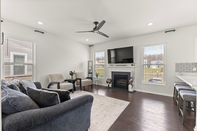 living room with a glass covered fireplace, ceiling fan, recessed lighting, and dark wood-type flooring