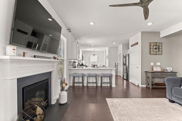 living area with a glass covered fireplace, baseboards, recessed lighting, a ceiling fan, and dark wood finished floors