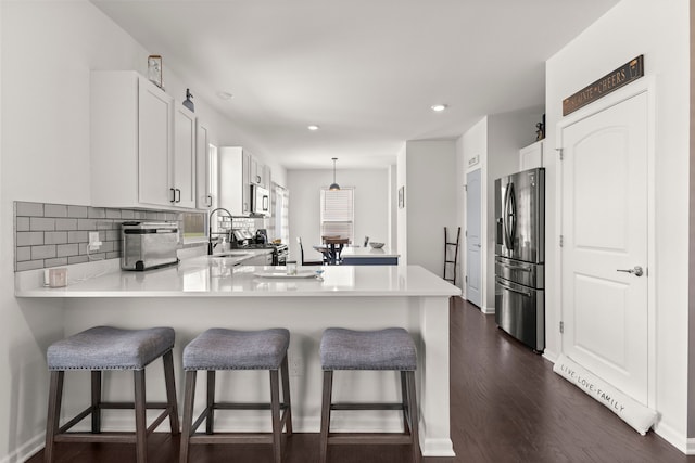 kitchen featuring a kitchen bar, appliances with stainless steel finishes, a sink, light countertops, and a peninsula