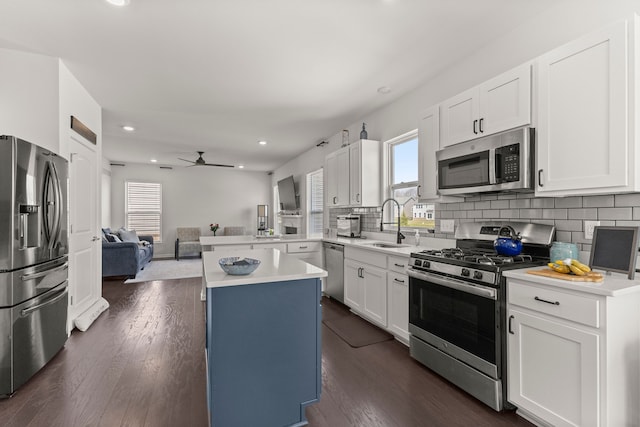 kitchen with a sink, light countertops, stainless steel appliances, open floor plan, and tasteful backsplash
