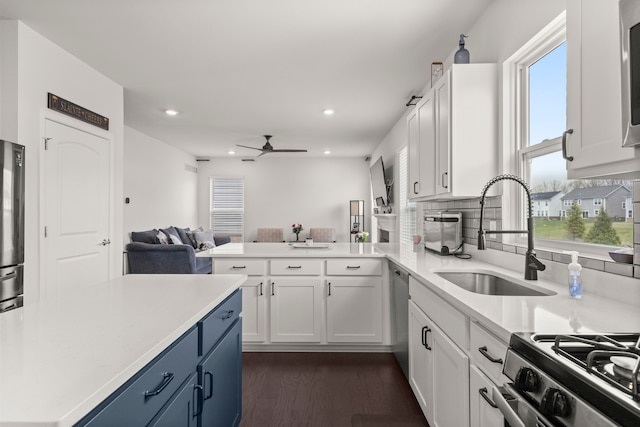 kitchen with open floor plan, ceiling fan, light countertops, white cabinetry, and a sink