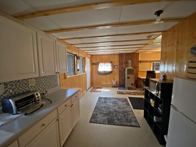kitchen with freestanding refrigerator, a wood stove, wood walls, and white cabinetry