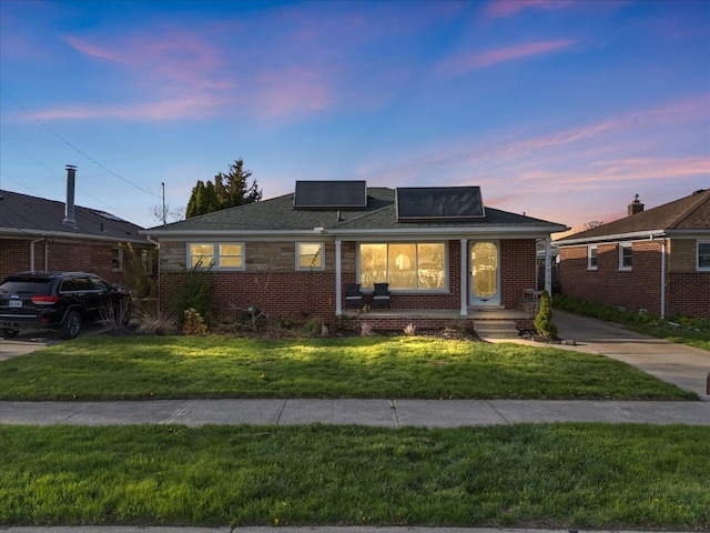 bungalow-style home with brick siding, a front lawn, and solar panels
