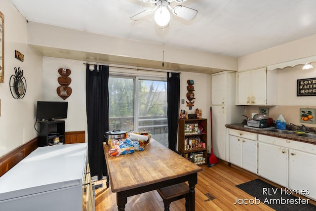kitchen featuring dark countertops, a sink, light wood finished floors, white cabinetry, and a ceiling fan