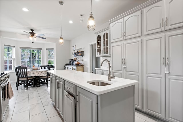7891 Robindale Ave, Dearborn Heights, MI 48127 - kitchen featuring a sink, gray cabinets, an island with sink, ceiling fan, and glass insert cabinets